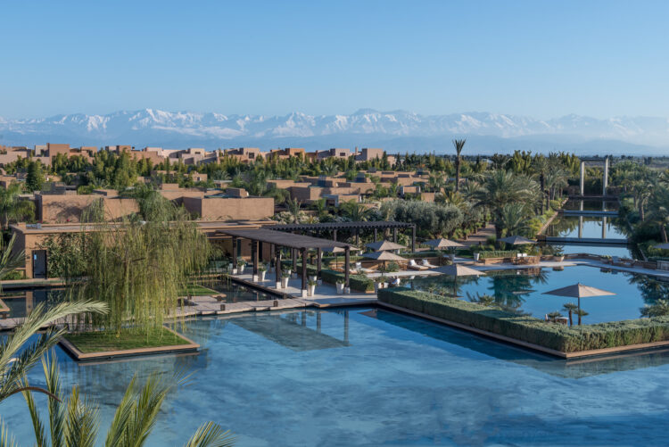 Vue sur les piscines et les villas ocre du Mandarin Oriental Marrakech sur fond de montagnes enneigées de l'Atlas au Maroc
