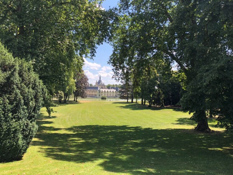 Grand parc boisé avec au fond une élégante bâtisse au toit d'ardoise, l'Auberge du Jeu de Paume à Chantilly
