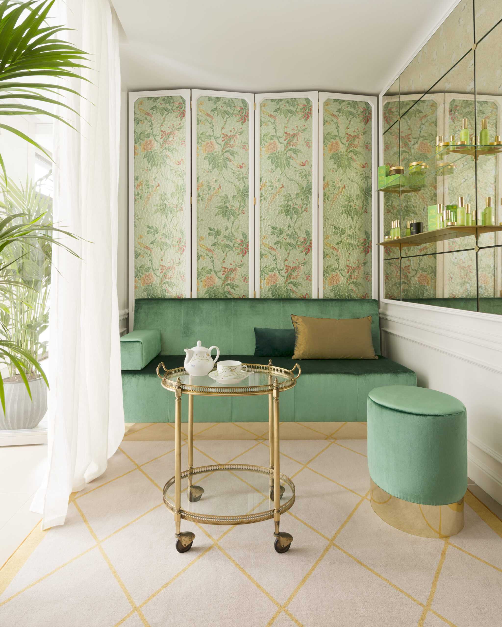 un petit salon Tata Harper au Spa Le Bristol by La Prairie avec du papier peint fleuri et un canapé en velours vert