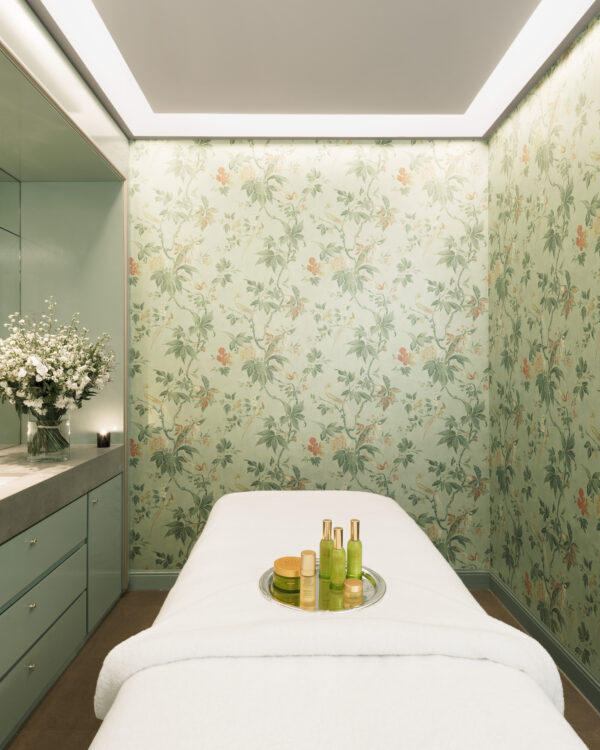 une cabine de soins Tata Harper au Spa Le Bristol by La Prairie avec une table de massage, des pot de crème et un bouquet de fleurs