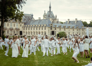 Des hommes, des femmes et des enfants habillés en blanc qui dansent sur l'herbe lors du pique en blanc organisé au château de Chantilly