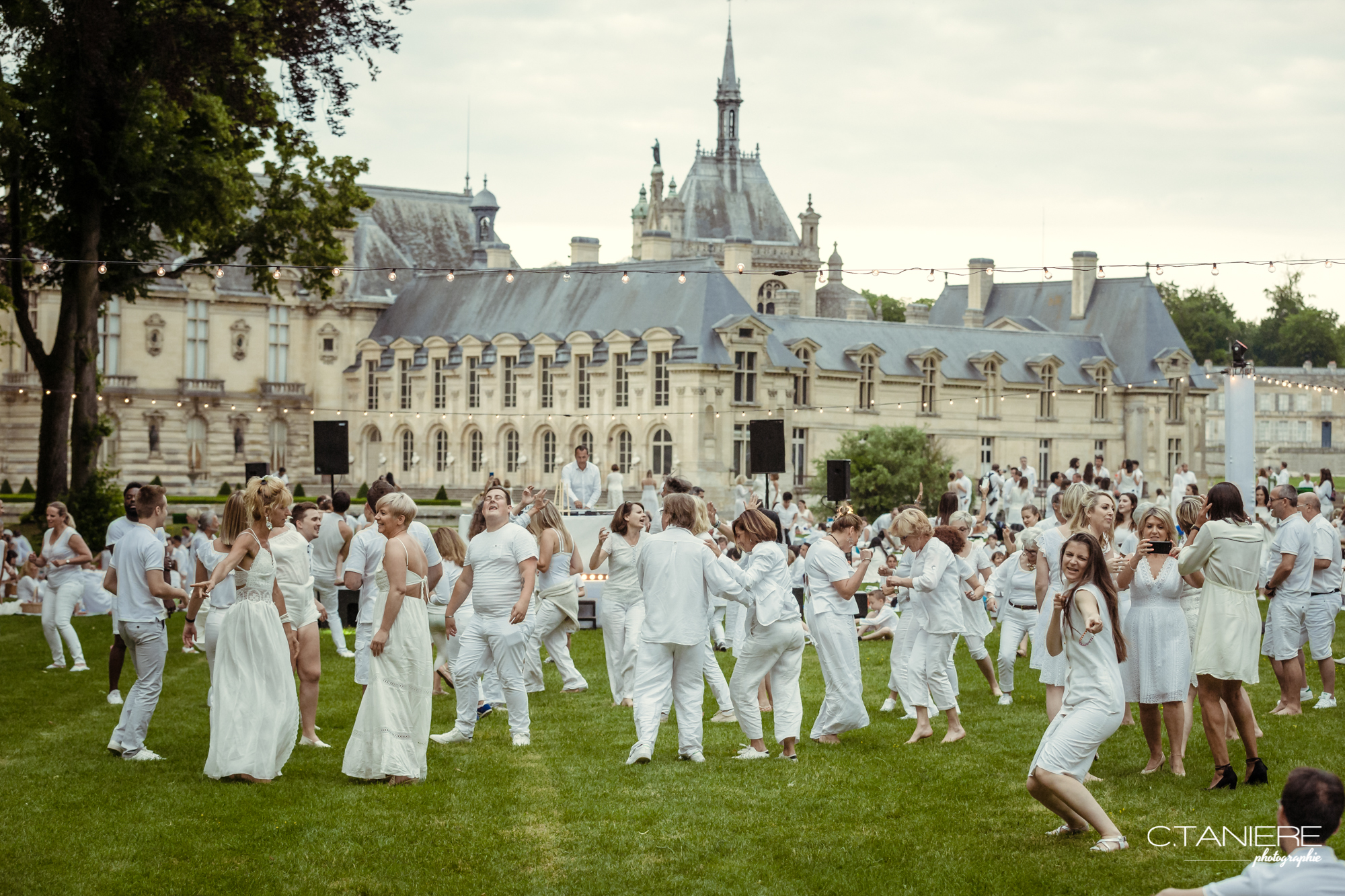 Des hommes, des femmes et des enfants habillés en blanc qui dansent sur l'herbe lors du pique en blanc organisé au château de Chantilly