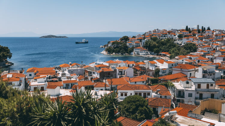 Vue depuis une colline, de maisons blanches aux toits orangés bordant un littoral rocheux, au bord de la mer Egée, sur l'île de Skiathos, en Grèce