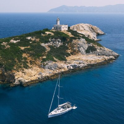 Une presqu'île rocheuse de Skiathos, avec un phare, et un voilier voguant sur l'eau de bleue de la mer Egée, en Grèce