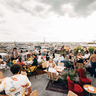 Le toit terrasse du rooftop Créatures à Paris avec plein de personnes en train de discuter et de boire un verre avec une vue sur les toits de Paris, l'Opéra Garnier et la Tour Eiffel