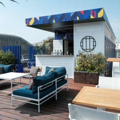 Vue de la terrasse du rooftop du Molitor à Paris, avec des canapés, des plantes vertes et un bar en bois blanc