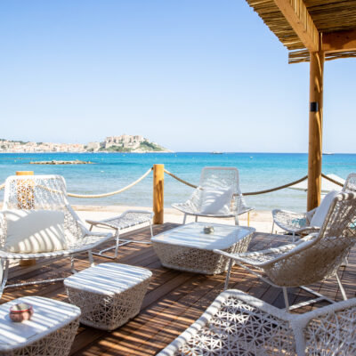 Une terrasse avec des fauteuils design blancs sur la plage de Calvi, face aux maisons de la ville et la citadelle