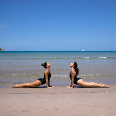 Deux jeunes femmes sur la plage de Calvi, en position de renforcement musculaire, lors d'une retraite Pilates à La Villa Calvi