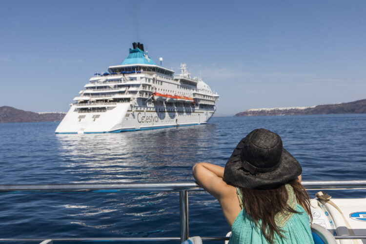 Une jeune femme vue de dos et portant un chapeau de paille, qui regarde s'éloigner le Celestyal Crystal qui propose des croisières vers les îles grecques