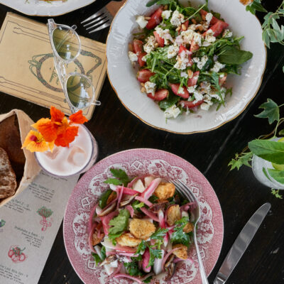 Assiettes anciennes fleuries servies avec une salade estivale sur le rooftop Créatures à Paris