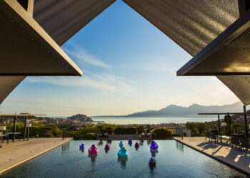 Un bassin à débordement avec des canards en plastique colorés, face à la mer et aux montagnes