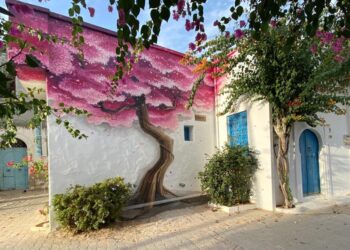 Ile de Djerba, au large de la Tunisie: une maison tradittionnelle blanche avec des portes bleues et un mur entièrement couvert d'une fresque représentant un arbre aux fleurs mauves