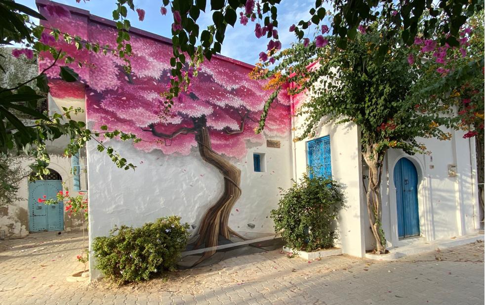 Ile de Djerba, au large de la Tunisie: une maison tradittionnelle blanche avec des portes bleues et un mur entièrement couvert d'une fresque représentant un arbre aux fleurs mauves