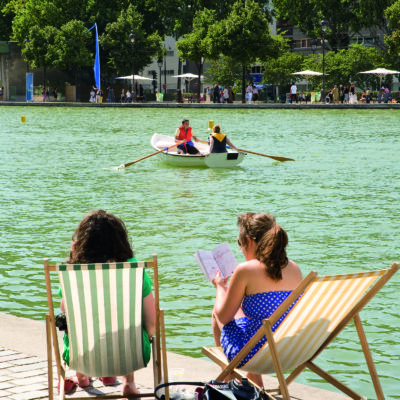 Deux jeunes filles assises sur des chaises longues en train de lire au soleil face au bassin de la Villette, lors de Paris Plage