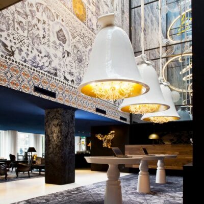 Salon de l'hôtel Andaz Amsterdam, avec d'énormes luminaires blancs, des fresques et grandes tables en marbre rondes