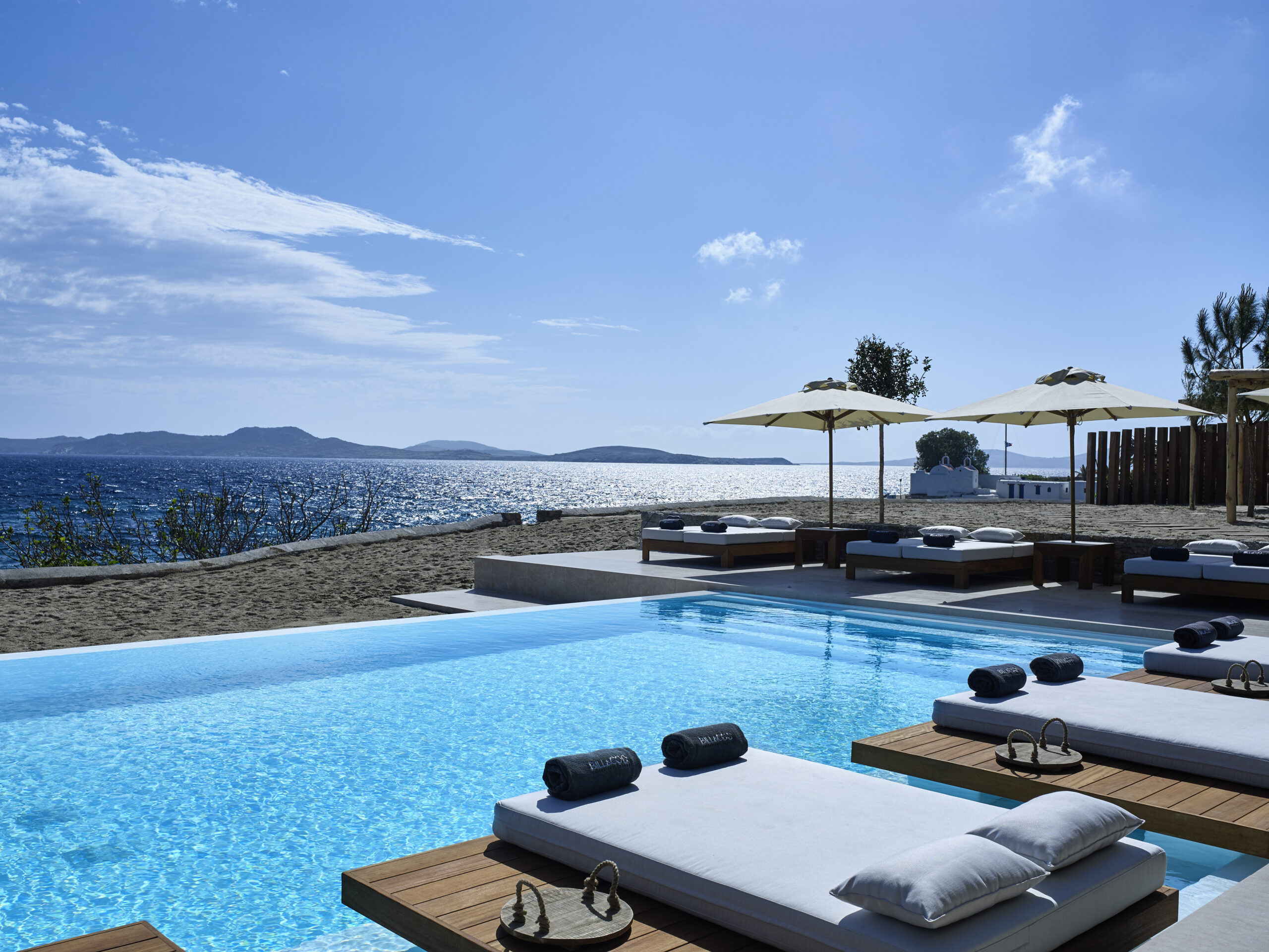 Une piscine entourée de transats et de sunbeds, au bord de la mer Egée, à l'hôtel Bill & Coo où se trouve l'une des plus belles piscines de Mykonos