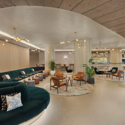 Photo de l'un des salons d'un hôtel Hilton de Londres en Grande Bretagne avec des canapés arrondis et verts sombres le long des murs, des tables et chaises design style années 50, et un grand bar au fond