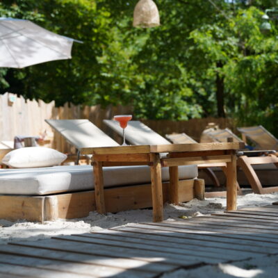 Des chaises longues et sunbeds sous des arbres et des parasols, alignés sur le sable de la Beach Parisienne, une plage privée à Paris