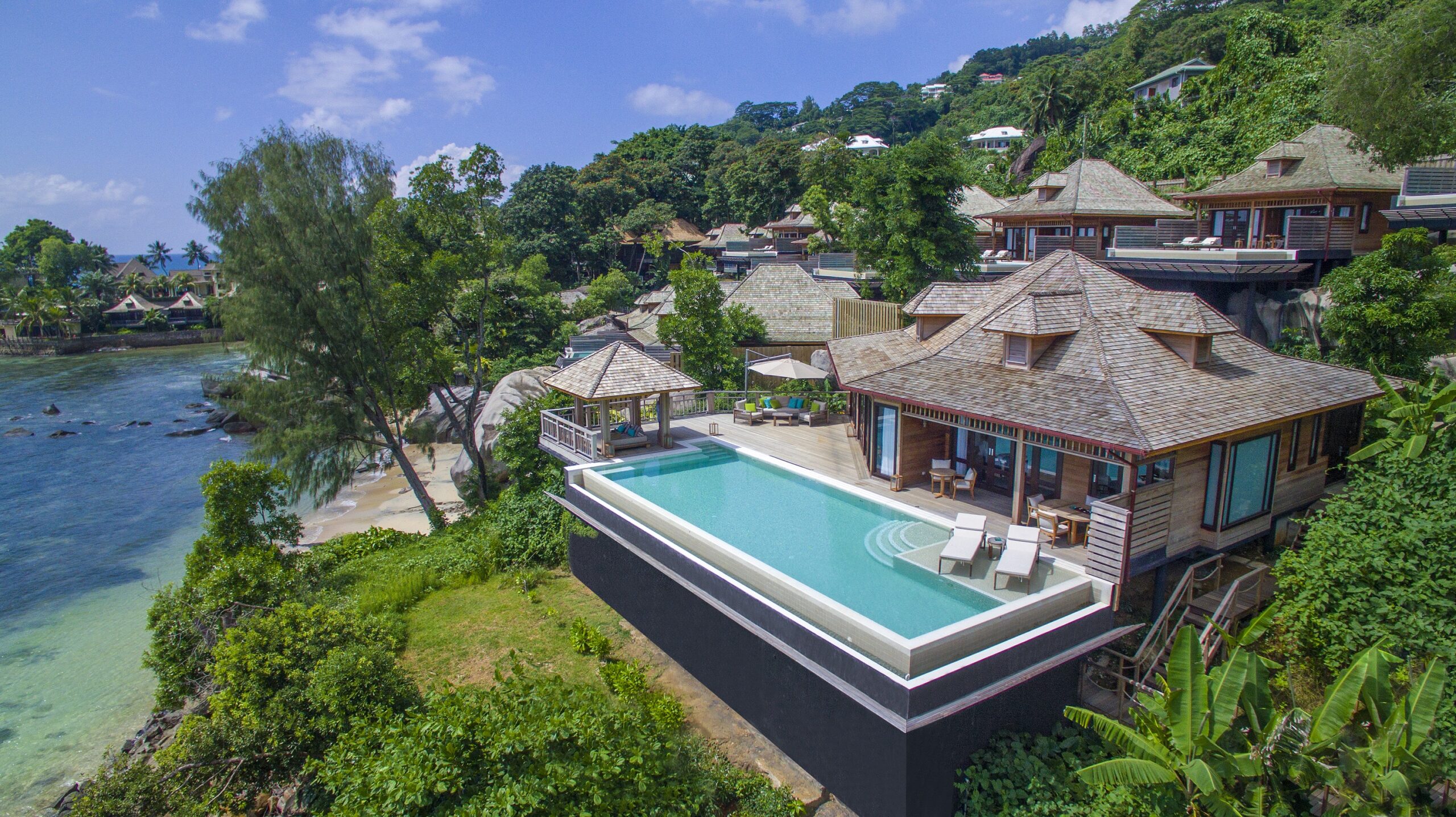 Vue aérienne d'une villa de type créole d'un hôtel Hilton aux Seychelles, avec une grande piscine privée, des transats, une végétation tropicale, au bord de l'océan Indien