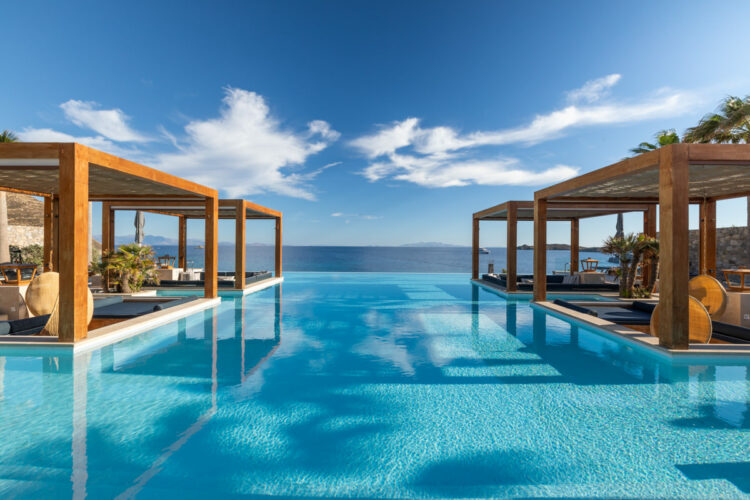 Vue de l'une des plus belles piscines de Mykonos, l'Oasis Pool du Santa Marina, une longue piscine en forme de T qui s'élance vers la mer Egée, elle est entourée de terrasse creusées au ras de l'eau bleue, avec de confortables canapés