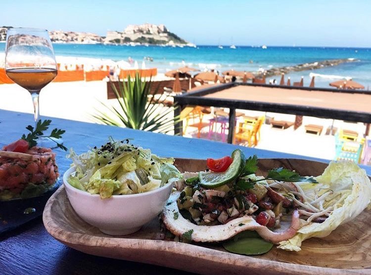 Une assiette de fruits de mer accompagné d'une salade et d'un verre de vin, sur une table face à la mer et à la citadelle de Calvi, à l'Octopussy, l'un des meilleurs clubs de plage de l'été
