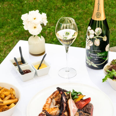 Au Trianon Palace Versailles, une table dressée avec une nappe blanche, un plat de viandes, des frites et une bouteille de champagne