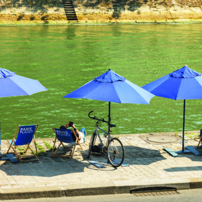 Un quai de la Seine à Paris, avec des parasols bleus et des chaises longues bleues avec écrit Paris Plage