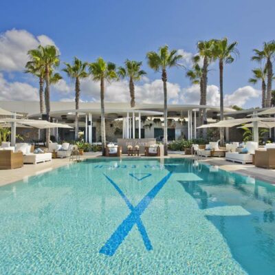 Une longue piscine bleue entourée de sunbeds blancs et de palmier, au Nikki Beach Marbella, l'un des meilleurs clubs de plage de Méditerranée