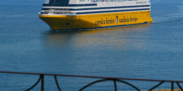 Une terrasse sur laquelle se trouve une table dressée pour le déjeuner, d'où l'on a une vue sur la mer et un navire de la Corsica Ferries