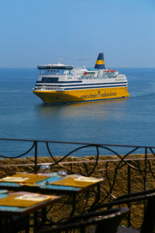 Une terrasse sur laquelle se trouve une table dressée pour le déjeuner, d'où l'on a une vue sur la mer et un navire de la Corsica Ferries 