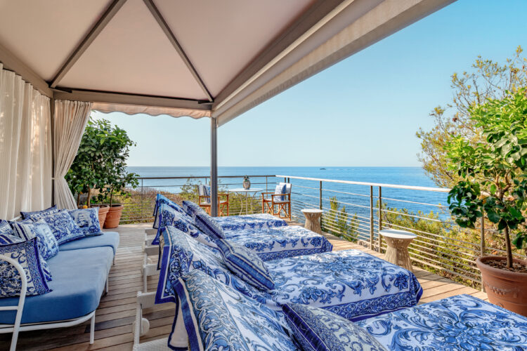 Vue d'une terrasse donnant sur la mer, avec des transats recouverts de tissus bleus imaginés par Dolce&Gabbana