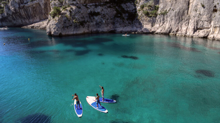 Trois personnes debout sur des paddles, sur une eau bleue transparente, près de Marseille