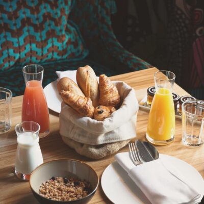 Une table dressée pour le petit déjeuner avec croissants, jus de fruits et bol de céréales, dans le restaurant de La Guitoune, adresse réputée du bassin d'Arcachon