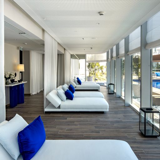 Des sunbeds blancs aux coussins bleus alignés sous une galerie, près de la grande piscine de l'Hôtel Martinez à Cannes