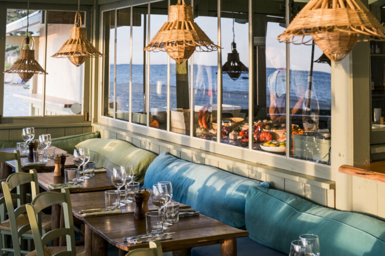 L'intérieur de la cabane Bartherotte du Club de Plage Pereire à Arcachon, avec des tables dressées pour le déjeuner, entourées de coussins bleus et verts