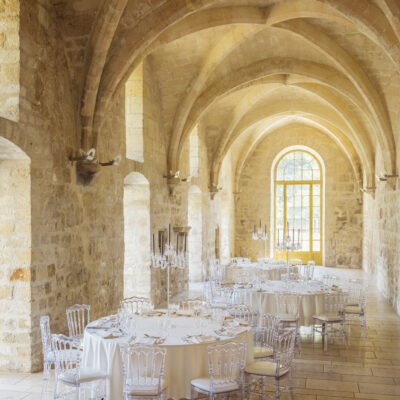 Une nef de l'abbaye de Royaumont reconvertie en salle de restaurant, avec de hautes voûtes, des fenêtres en ogives et des tables rondes nappées de blanc, dressées élégemment