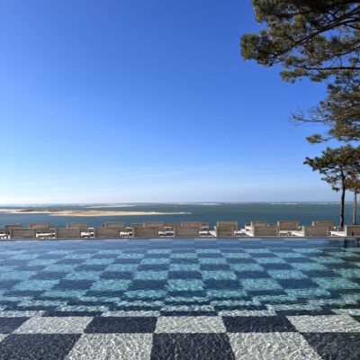 Vue de la piscine de La Co(o)rniche, dont le fond en damier noir et blanc tranche avec le bleu du ciel et du bassin d'Arcachon qu'elle domine de toute sa hauteur