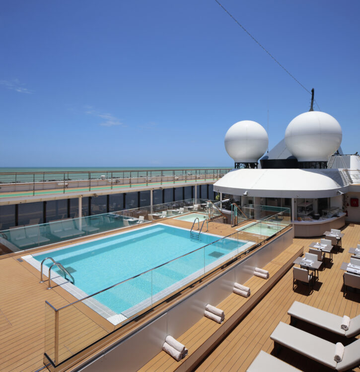 Vue du pont supérieur du World Explorer qui propose une croisière musicale, avec une grande piscine sur un pont en bois, entourée de transats