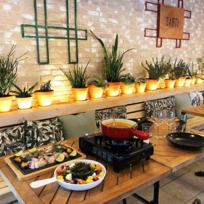 Vue intérieure du restaurant le Sarti sur l'île des Embiez, avec des cactus sur une longue étagère et une table en bois avec des assiettes de poisson cru, une soupe provençale et une salade de légumes colorés