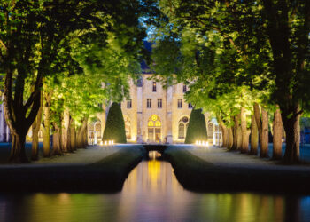 Une vue nocturne de l'abbaye de Royaumont, avec une allée qui entoure un bassin menant à la batisse