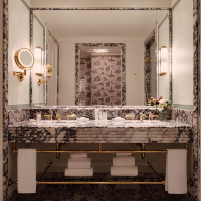 New York: une salle de bain de l'Hôtel Barrière Fouquet's New York, avec du marbre noir et blanc, de la robinetterie dorée et en vue dans le miroir, le papier en toile de Jouy US style
