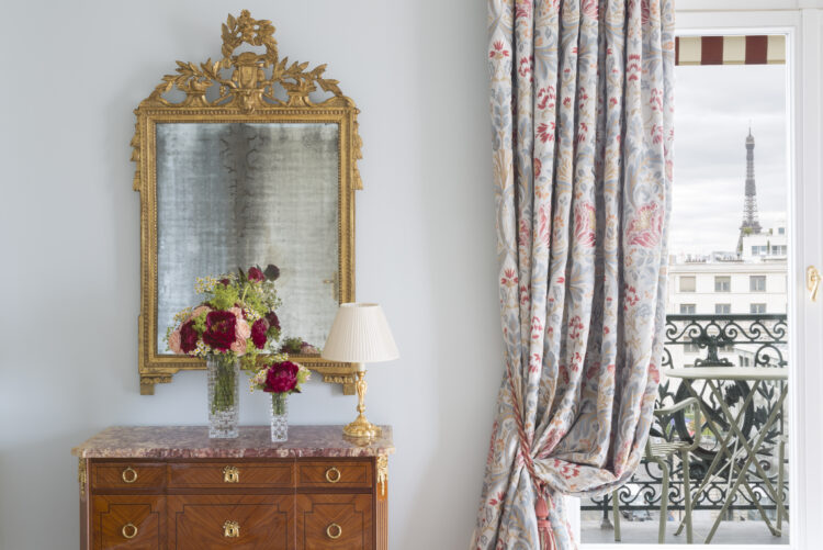 La Suite Paris de l'hôtel Le Bristol Paris, avec une commode marquetée au plateau de marbre rose, surmonté d'un miroir doré, mobilier placé juste à côté d'une haute fenêtre avec vue sur la Tour Eiffel