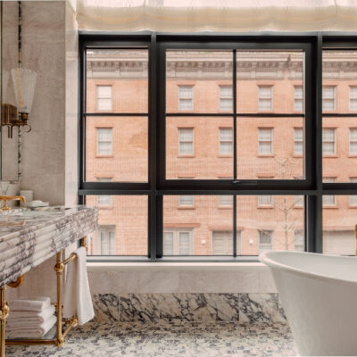 New York: une salle de bain de l'Hôtel Barrière Fouquet's New York, avec une grande fenêtre avec vue sur un immeuble typique en briques, du marbre noir et blanc, de la robinetterie dorée et une large baignoire sur pied