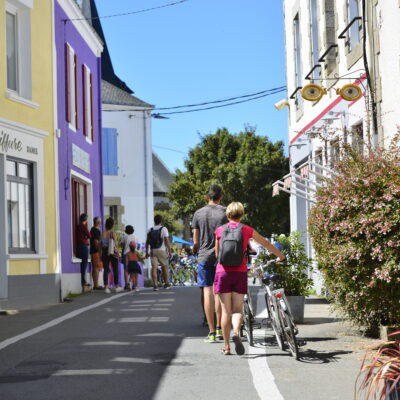 Des touristes qui se baladent à pied et à vélo dans les rues bordées de maisons colorées du village Le Bourg, sur l'île de Groix