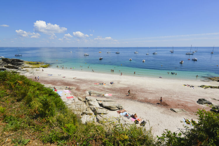 Vue sur le sable poudré de tons ocre de la plage Les Sables Rouges, au bord d'un océan Atlantique qui, aux abords l'île de Groix, prend les teintes turquoise d'un lagon breton