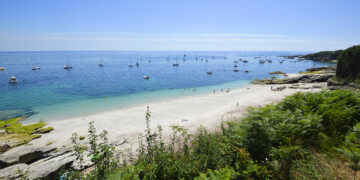 Vue, depuis le sentier de la plage Les Grands Sables sur l'île de Groix, avec son sable fin qui semble fondre dans la mer aux dégradés de bleus turquoise et indigo