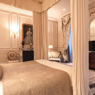 Une chambre du Relais & Château Domaine Les Crayères, décorée dans un style 18e classique avec lit à baldaqui, fauteuils et commode Louis XVI et toiles de maîtres