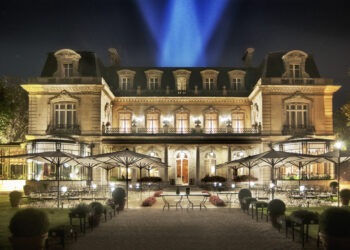 La façade en U du Relais & Château le Domaine Les Crayères éclairé de nuit, avec ses balcons en fer forgé et sa terrasse ouverte sur un jardin à l'anglaise