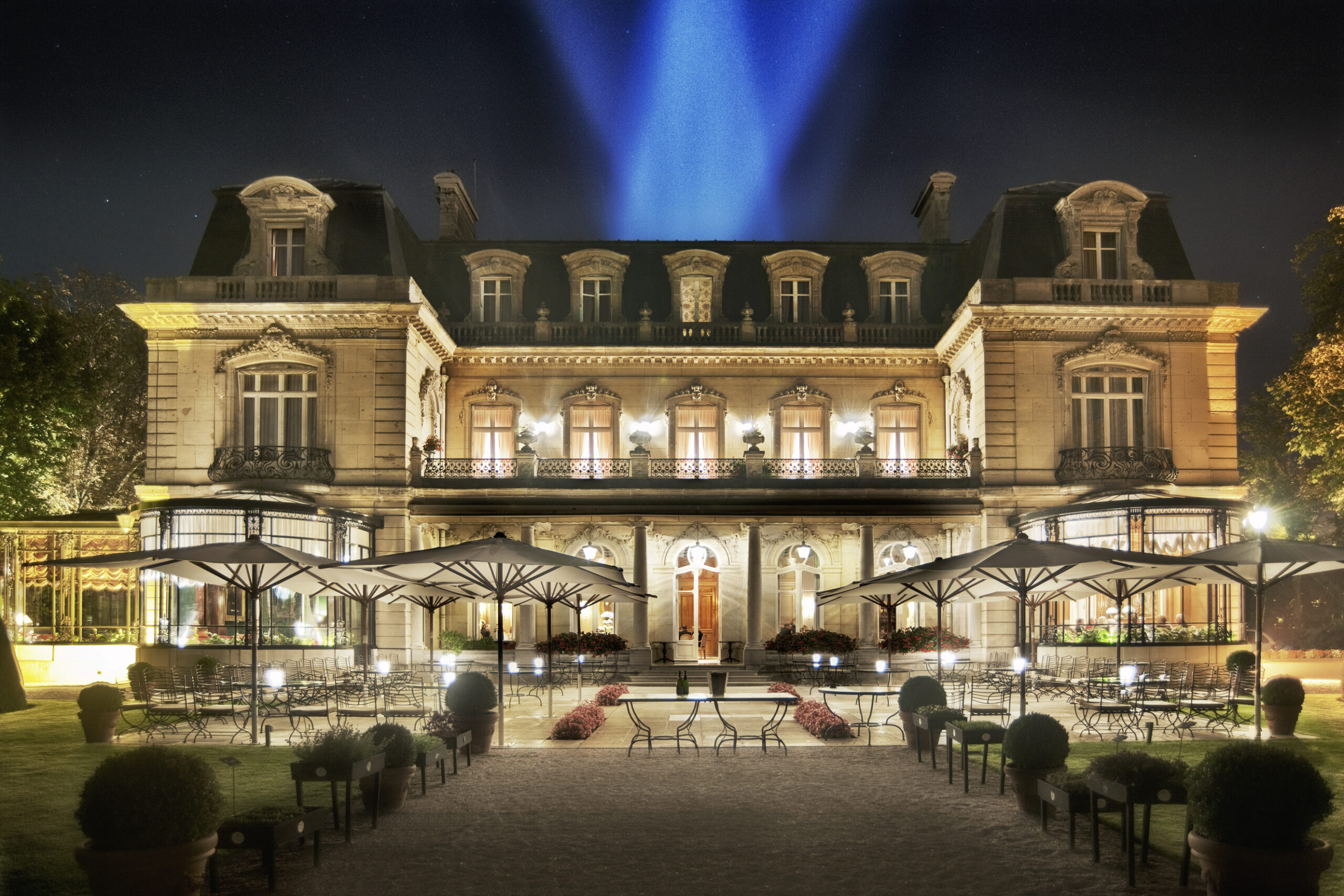 La façade en U du Relais & Château le Domaine Les Crayères éclairé de nuit, avec ses balcons en fer forgé et sa terrasse ouverte sur un jardin à l'anglaise