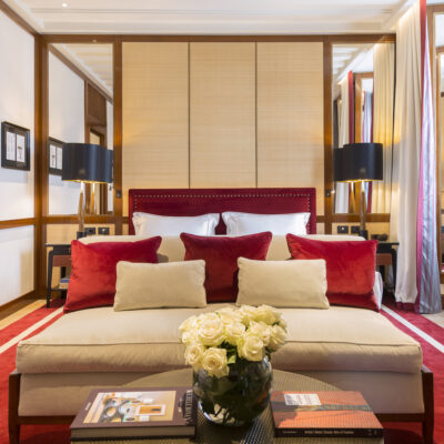Une chambre de style contemporain de l'hôtel Portrait Milano, avec un grand lit beige sur un tapis rouge, design contemporain, miroirs et bois sombres.